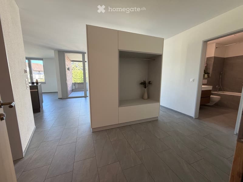 Modern hallway with tiled flooring, white walls, and open doors leading to a closet and bathroom. The closet contains a vase with plants, and the bathroom has a bathtub, toilet, and sink.