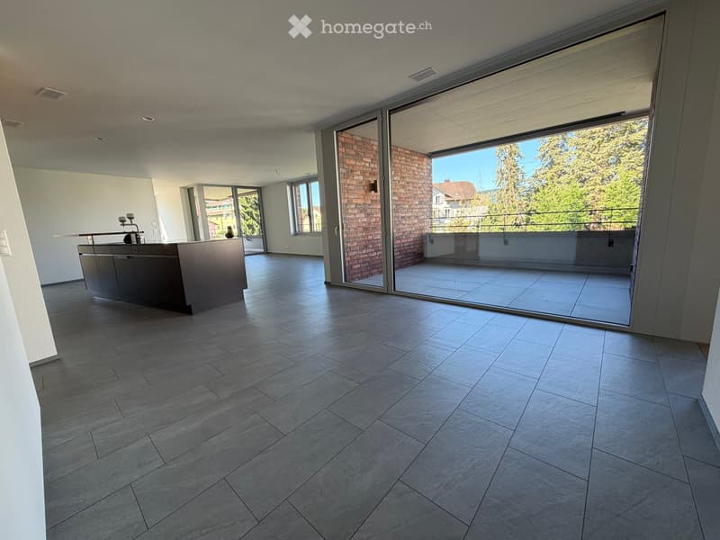 Modern, open-plan kitchen with grey tiled floor, large sliding glass doors leading to a balcony, and a central kitchen island.