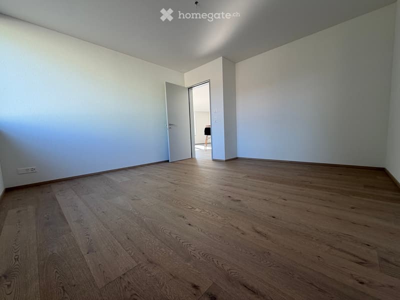 Empty room with light-colored walls and wooden flooring, featuring an open doorway leading to another room.