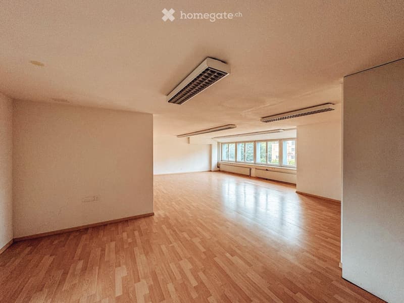 Empty room with wooden flooring, white walls, and large windows allowing natural light. No furniture or equipment present.