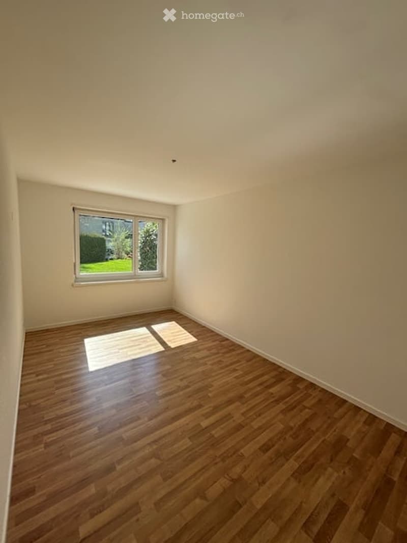Empty room with wooden flooring and a single window showing a view of greenery outside.