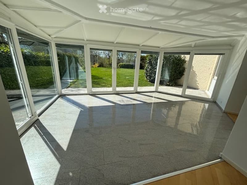 Empty conservatory with large glass windows and a polished concrete floor, allowing ample natural light.