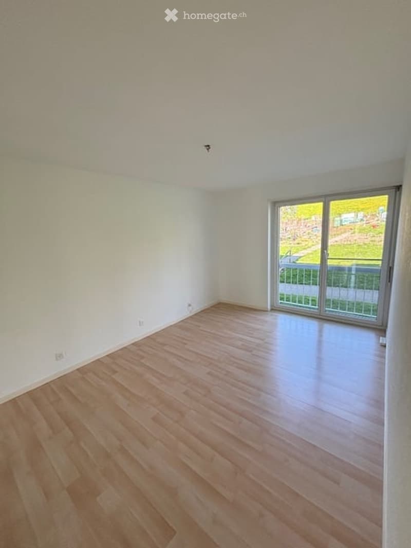 Empty room with wooden flooring, white walls, and large sliding glass door leading to a balcony.