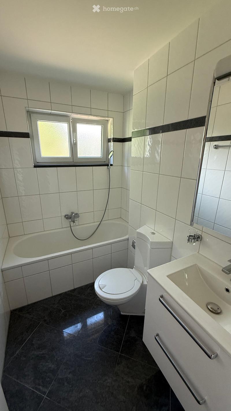 Modern bathroom with white tiles, a bathtub, toilet, sink, and a window above the bathtub.