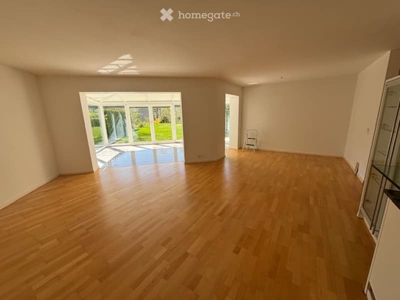 Empty room with wooden flooring, large glass door leading to a patio, and a small folding chair in the corner.
