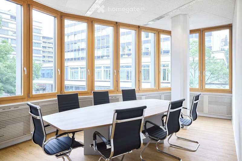 Bright conference room with large windows, a long white table, and several black chairs arranged around it.