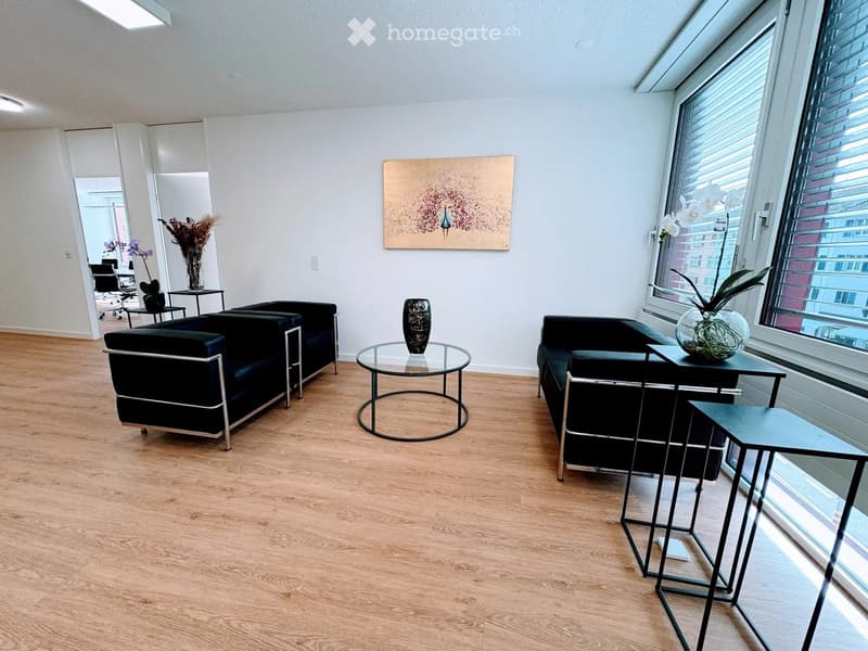 Modern, minimalist living room with light wooden flooring, large windows, and contemporary black furniture including a sofa, glass coffee table, and side tables.