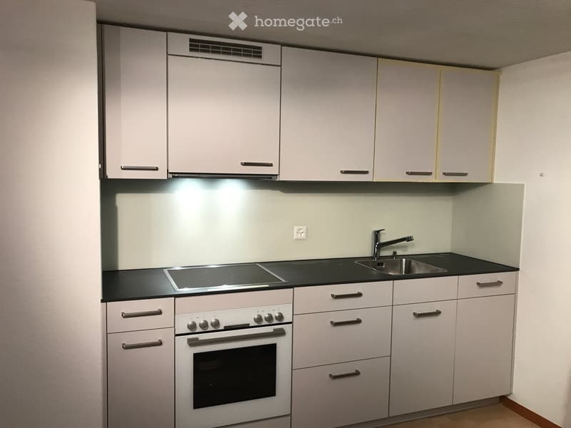 Modern kitchen with white cabinets, black countertops, an induction cooktop, an oven, and a sink with a faucet.