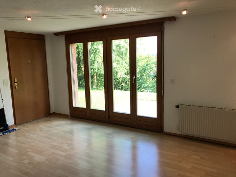 Empty room with wooden flooring, large sliding glass doors, and a radiator on the wall.