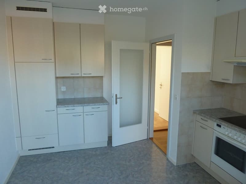 Modern kitchen with white cabinets, granite countertops, and built-in appliances including an oven and dishwasher. The space features a tiled backsplash and a doorway leading to another room.