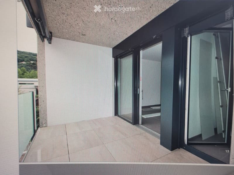 Modern balcony with large glass sliding doors, tiled floor, and a view of greenery outside.