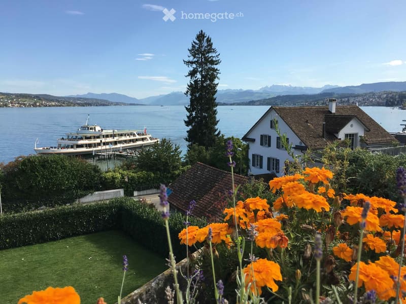 Garden with orange flowers and lavender, overlooking a lake with a docked boat and distant mountains.