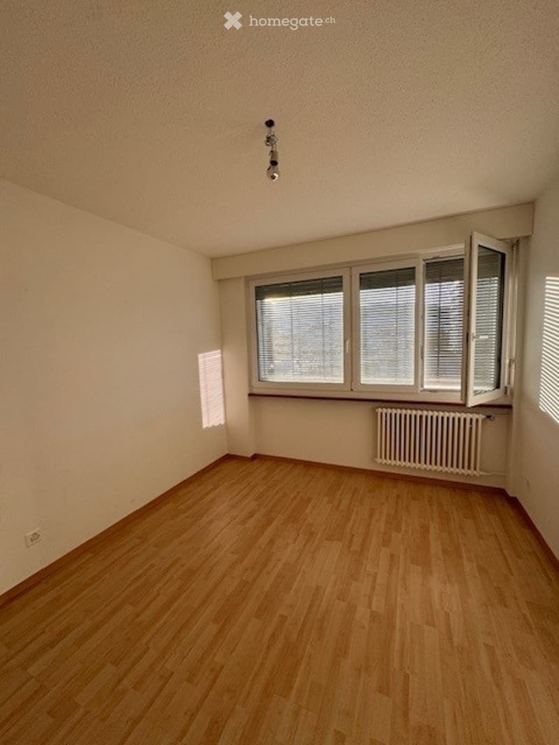 Empty room with wooden flooring, white walls, and large windows with blinds. No furniture or equipment present.
