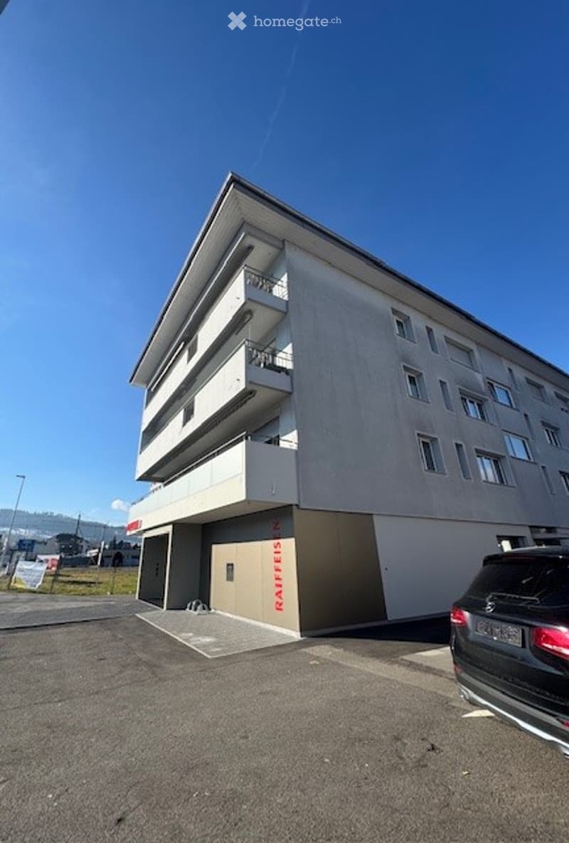 4 story apartment building, with a garage entrance on the ground floor, located on a busy road with a parking lot