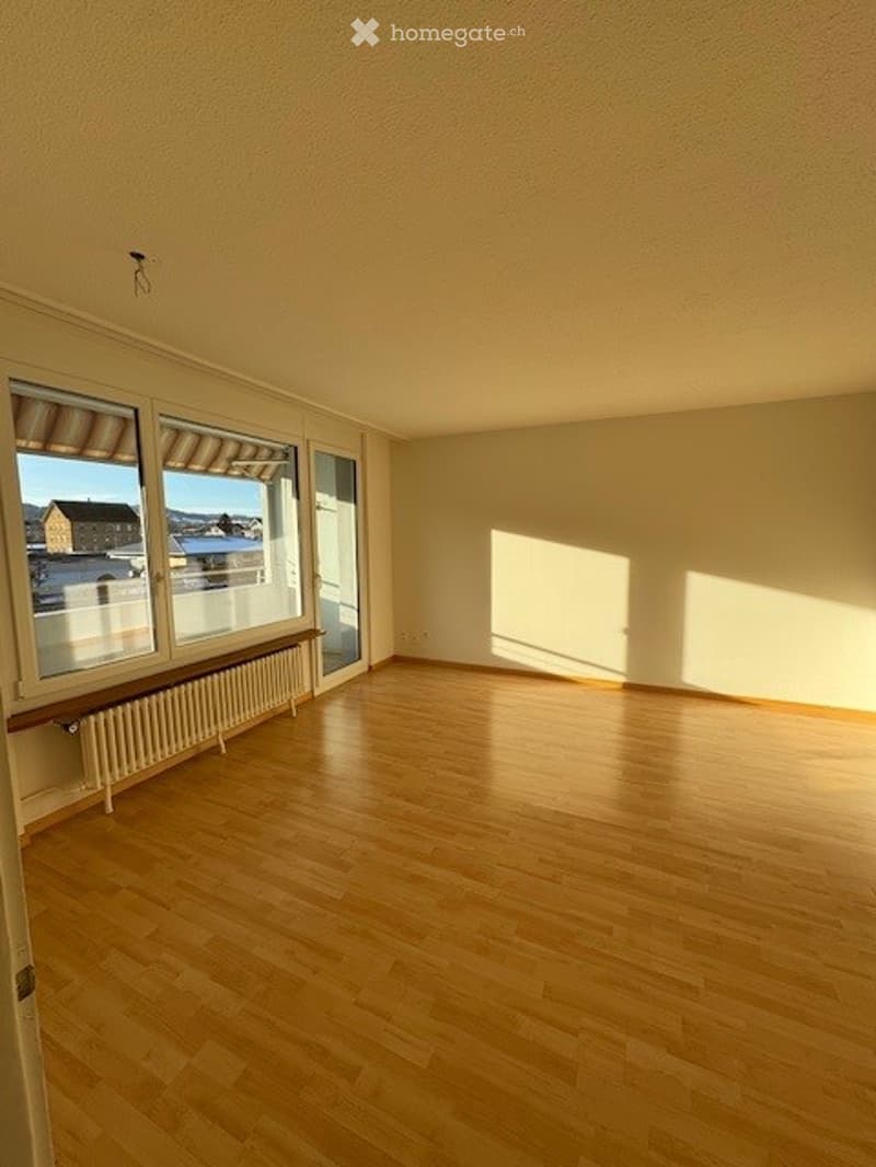 Empty room with wooden flooring, large windows with blinds, radiator, and a glass door leading outside.
