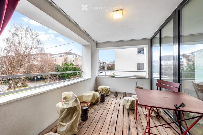 Balcony with wooden decking, glass railing, and a small table and chair set.