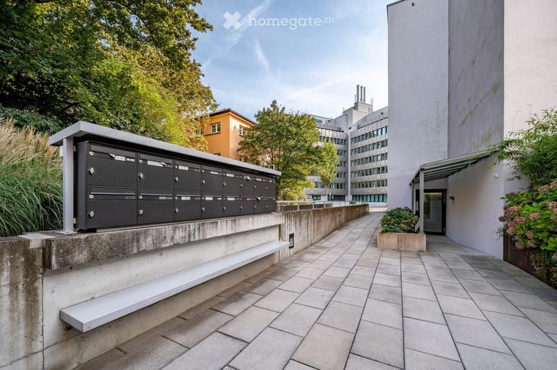 Modern outdoor area with tiled pavement, mailboxes, and surrounding greenery.