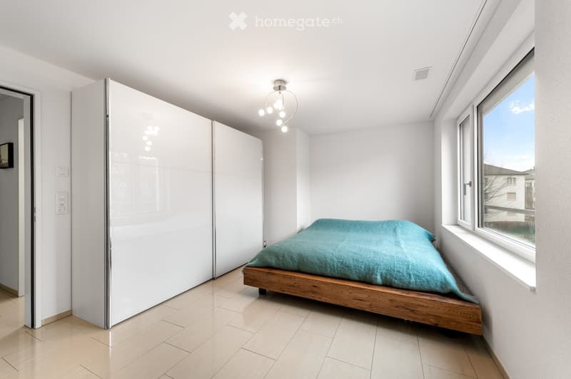 Modern bedroom with a wooden bed, teal bedding, large white sliding wardrobe, and large windows with a view.