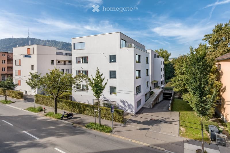 Modern multi-story residential building with white facade, balconies, and a covered garage entrance.