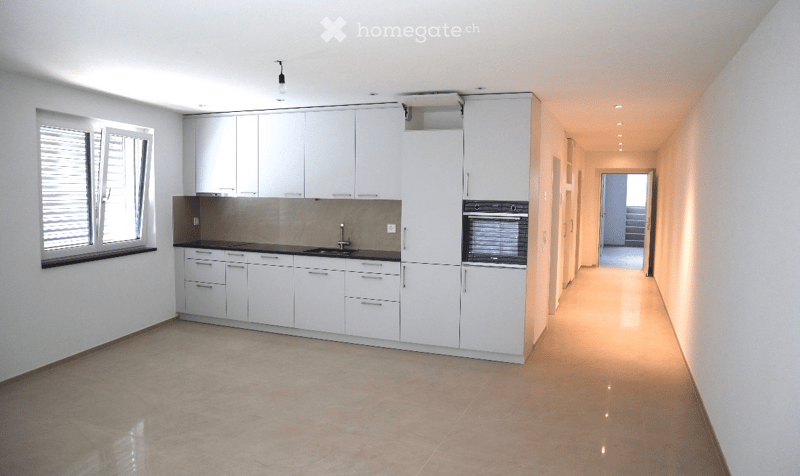 Modern kitchen with white cabinets, black countertops, and built-in appliances including a sink and oven. The space is clean and well-lit with natural light from a window on the left.