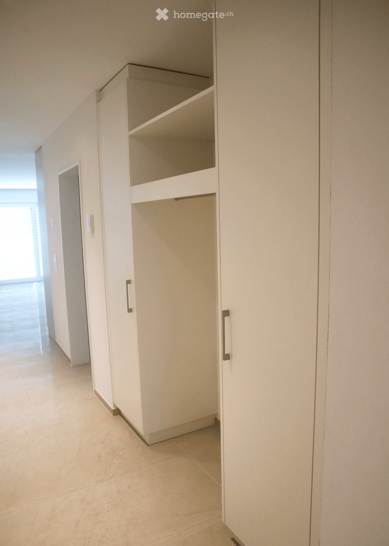 Empty room with white walls, light-colored tiled floor, and built-in white cabinet with empty shelves.