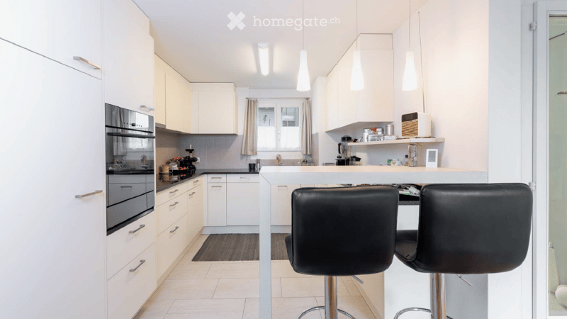 Modern kitchen with white cabinets, stainless steel appliances, island with bar stools, and various kitchen items on the counter.