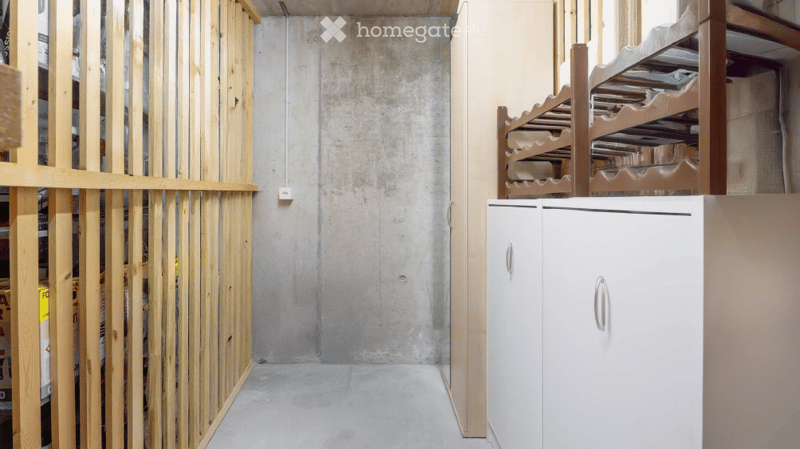 Empty room with exposed concrete walls and floor, white cabinet with double doors, wooden shelving unit, and wooden paneling on one side.