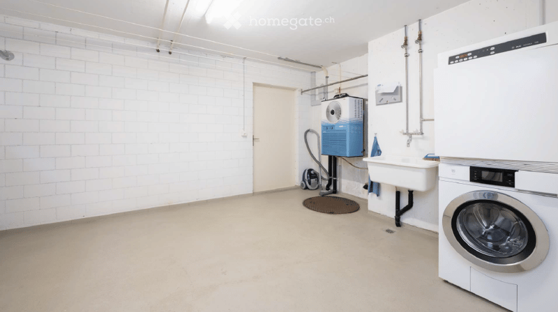 Empty room with white brick walls, concrete floor, and a private washing machine in the corner.