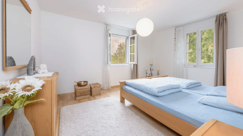Cozy bedroom with a wooden bed, white bedding, a large mirror, a vase with sunflowers, and decorative items on a shelf.