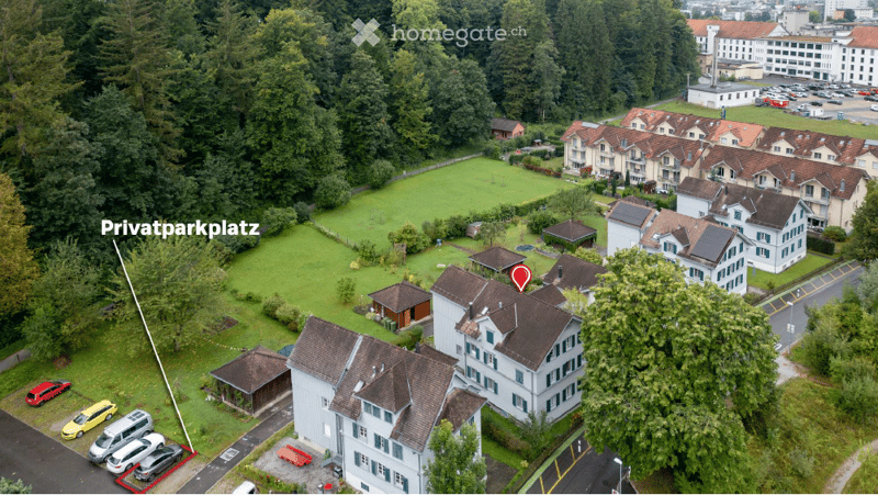 Aerial view of a residential complex with multiple buildings, surrounded by greenery and a private parking area.