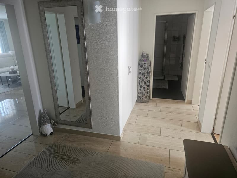 Hallway with tiled flooring, large mirror, small decorative items, and an open doorway leading to a bathroom.