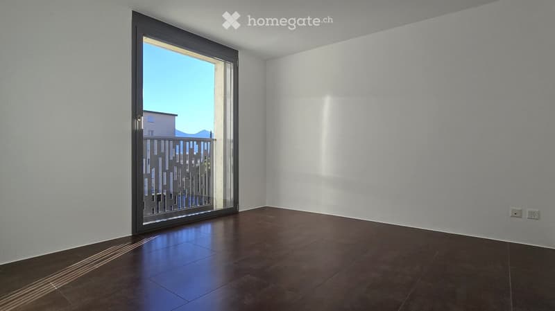 Empty room, white walls, sliding glass door to balcony, brown tiles, power outlets on the wall.