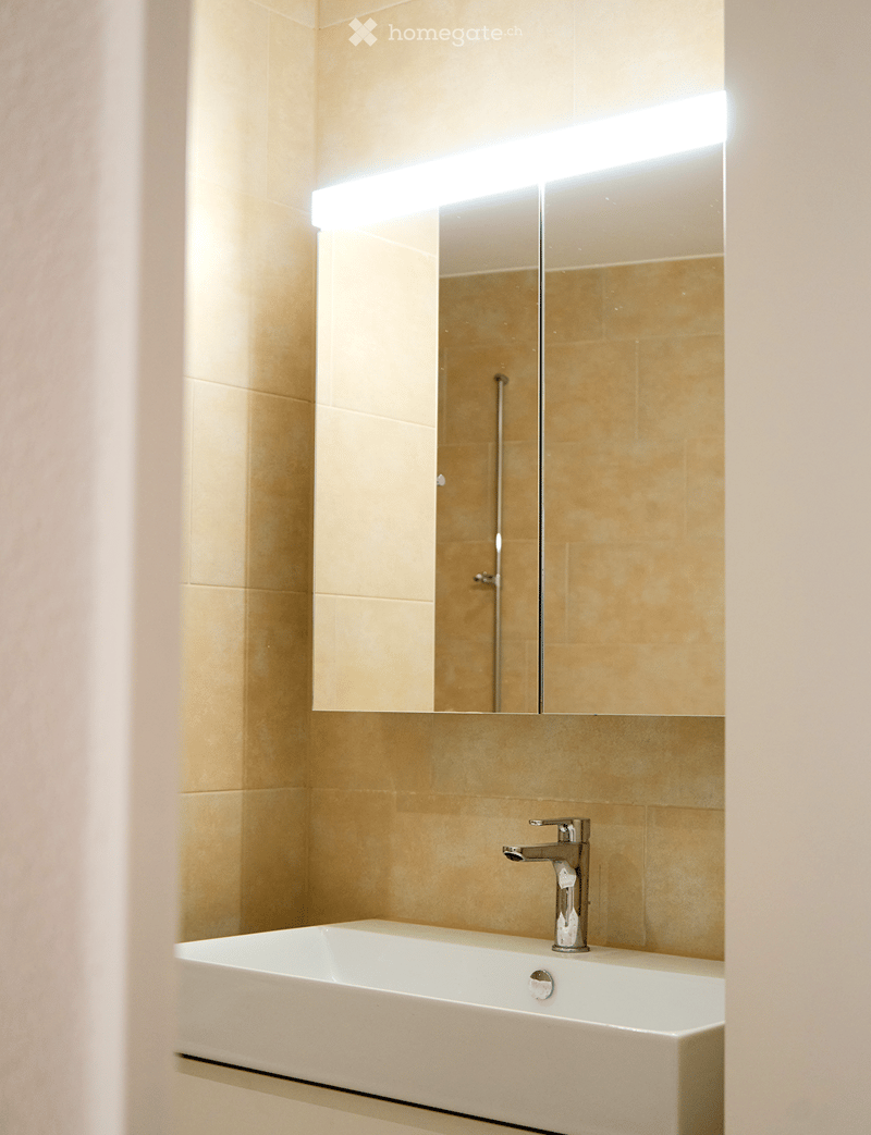 Modern bathroom with a white sink, chrome faucet, and large mirror with built-in lighting.