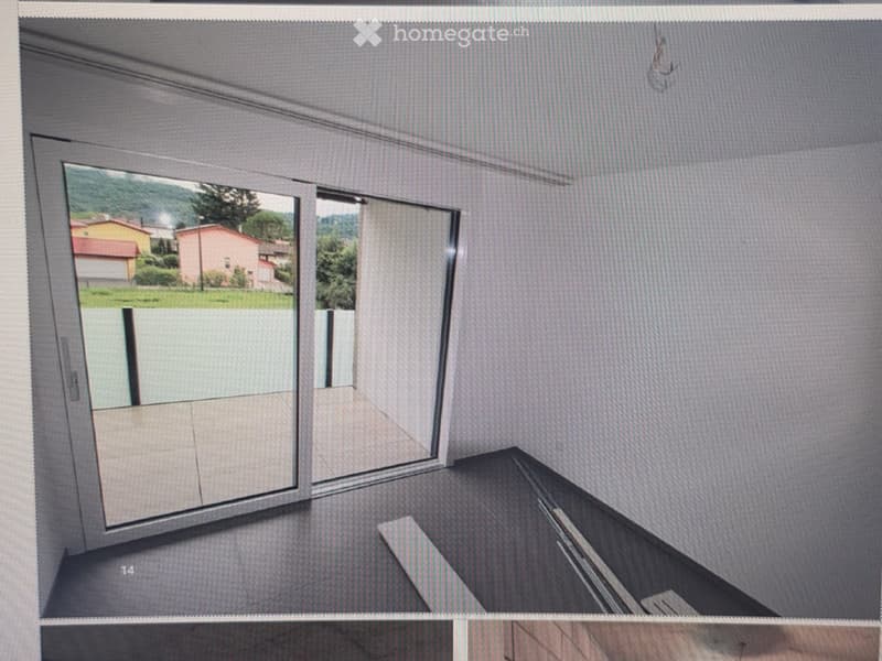 Empty room with grey walls, large window showing outdoor view, and a dark floor.