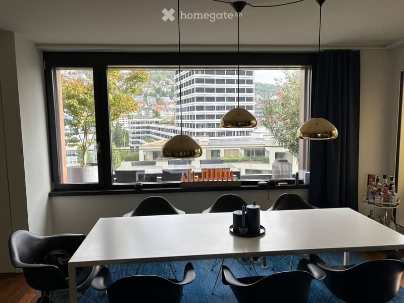 Modern room with a white table, black chairs, pendant lights, and a view of the cityscape through large windows.