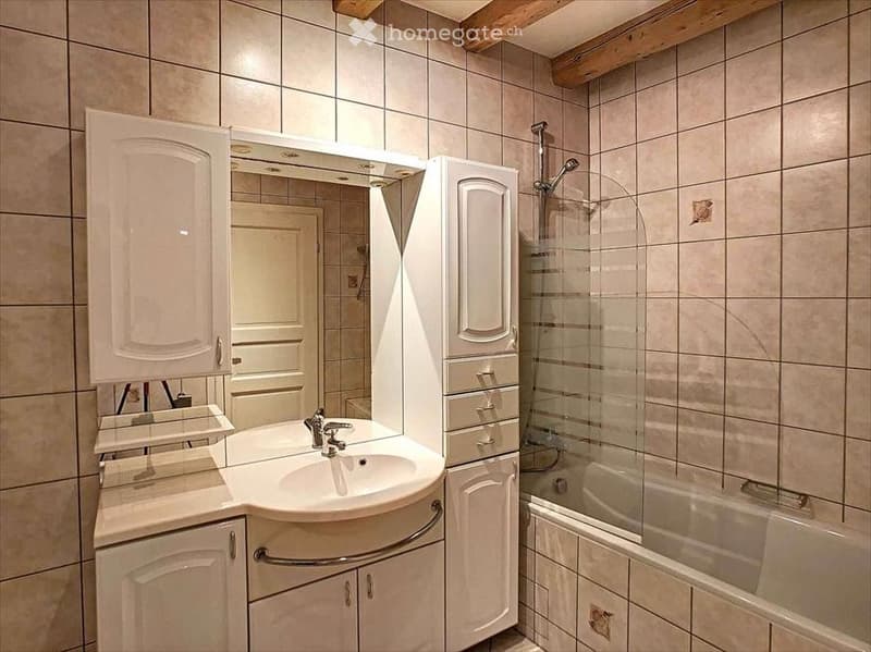 Bathroom with a white sink, mirror, bathtub, and shower area. The walls are tiled, and there are white cabinets and drawers.