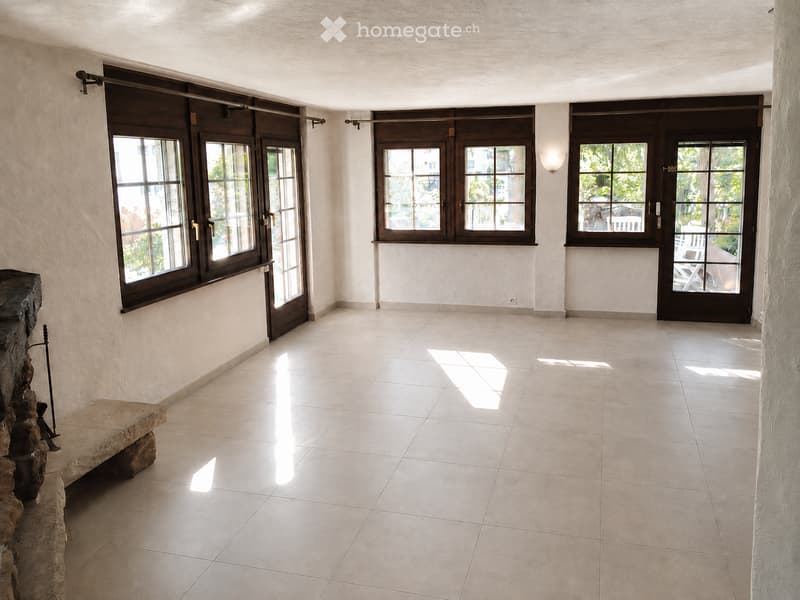 Empty room with tiled floor, large windows with dark frames, and a stone bench near the wall.
