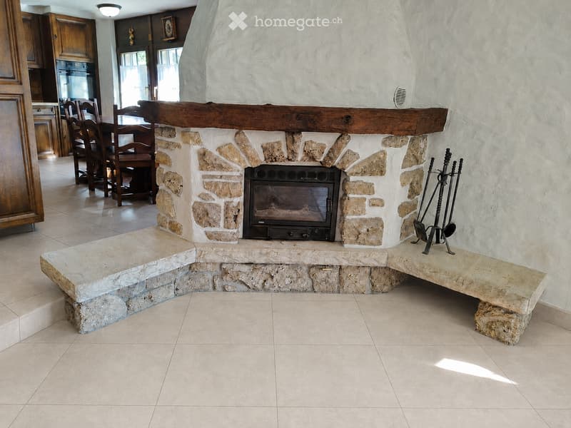 Stone fireplace with built-in seating, fireplace tools, and a dining area visible in the background.