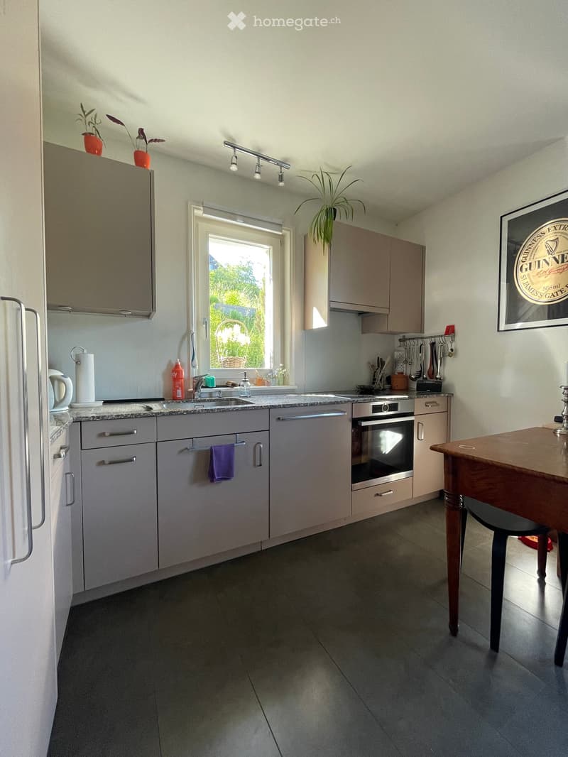 Modern kitchen with grey cabinets, stainless steel appliances, a central island, and a wooden dining table.