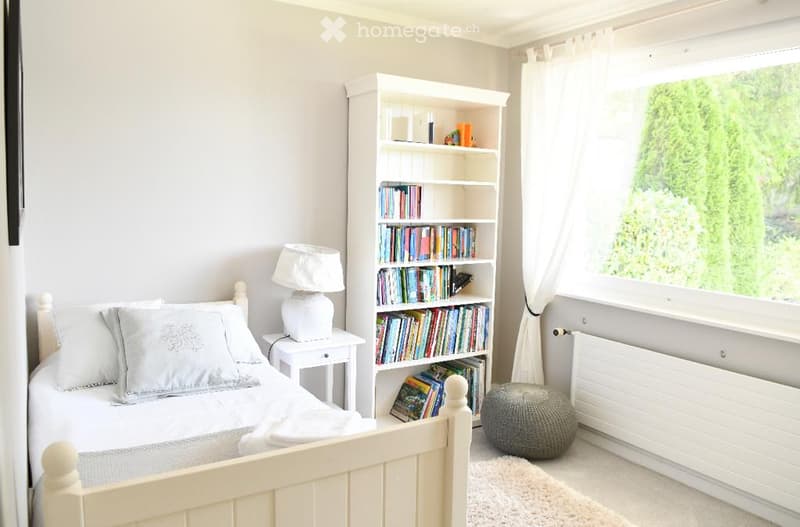Single bed, white nightstand, lamp, white bookcase, white rug, white curtains, window