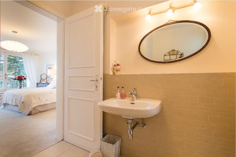 small bathroom with sink, mirror, and wicker basket, with view to bedroom