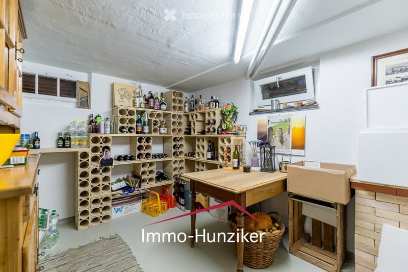 A well-organized wine cellar with a wooden table, wine racks filled with bottles, a refrigerator, a sink, and various decorative items including a lantern and a poster.