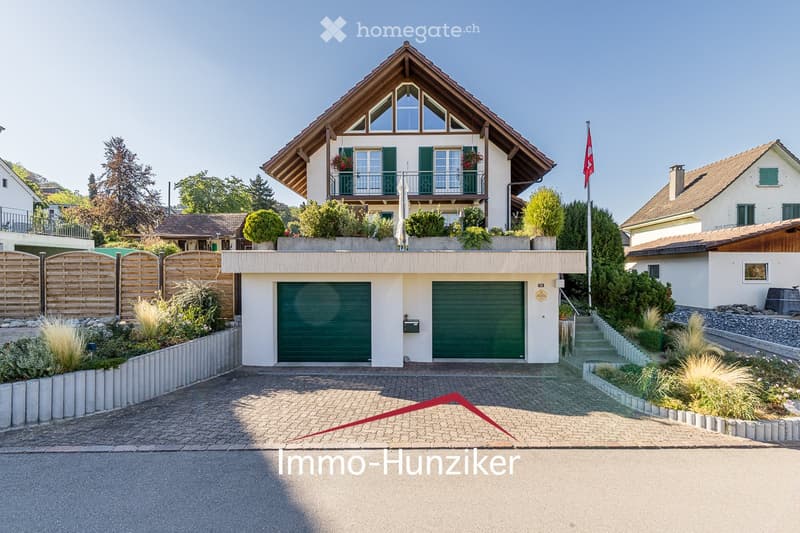 Two-story house with a garage, balcony, and well-maintained garden.