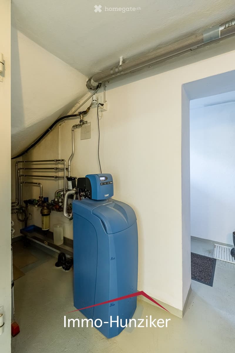 Utility room with a water softener unit, pipes, valves, and a control unit mounted on the wall.