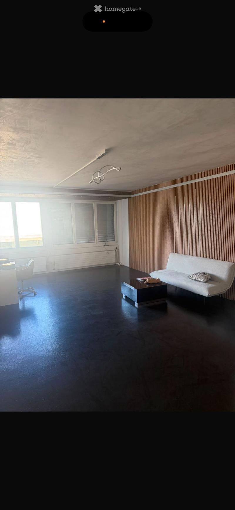 Modern living room with dark flooring, white sofa, coffee table, and a chair near the window.
