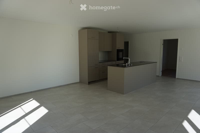 Modern kitchen with light-colored cabinets, a central island with a sink, and tiled flooring. The space is bright with natural light streaming in from an unseen window.