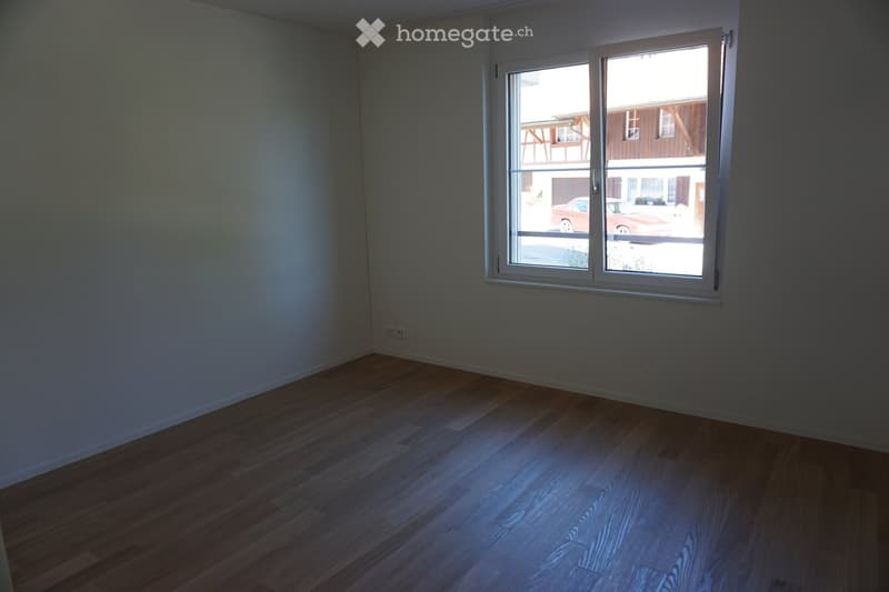 Empty room with wooden flooring and a large window offering a view of the street and neighboring buildings.