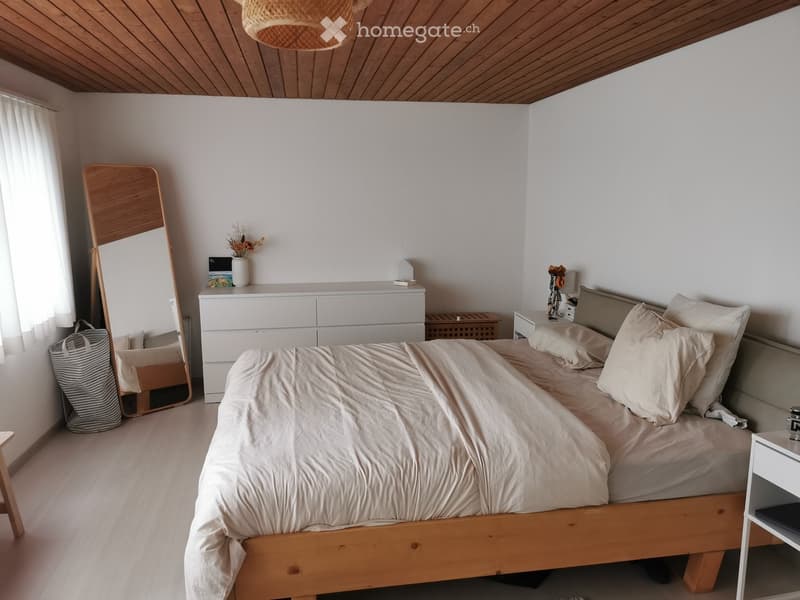 A modern, minimalist bedroom with a wooden bed, white bedding, a nightstand, a dresser, a mirror, and a vase on the dresser.