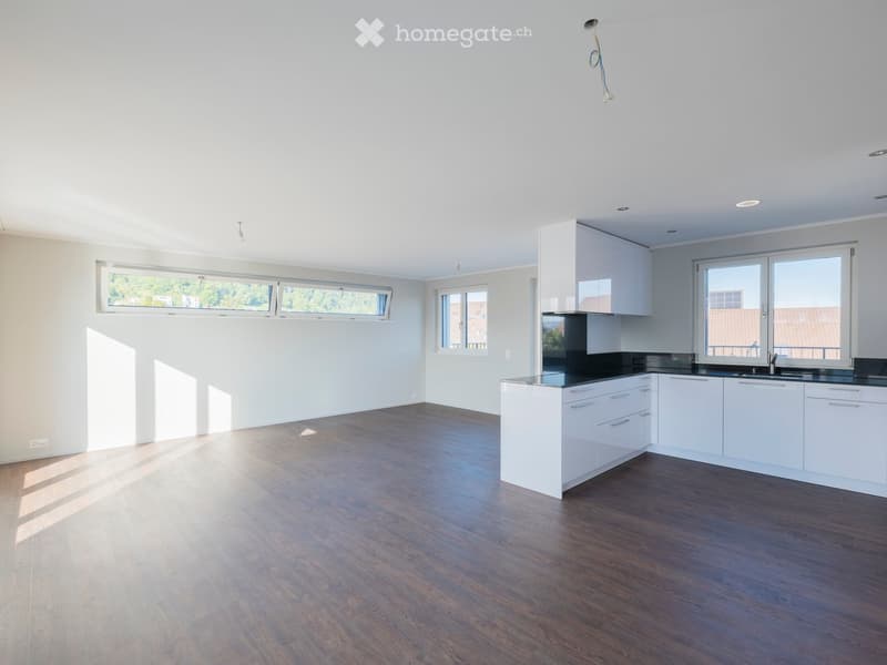 Empty kitchen with white cabinets, black countertops, and wooden flooring. Large windows allow natural light to fill the space.