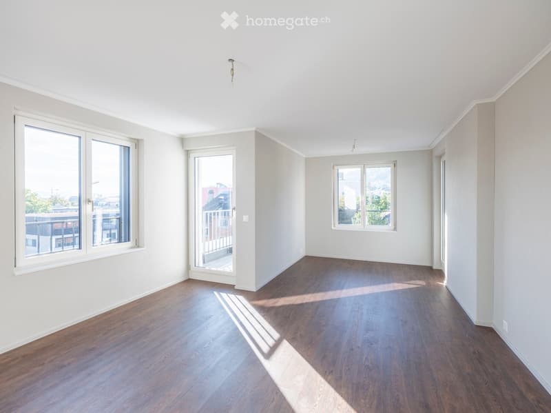 Empty room with wooden flooring, white walls, large windows, and a sliding glass door leading to a balcony.